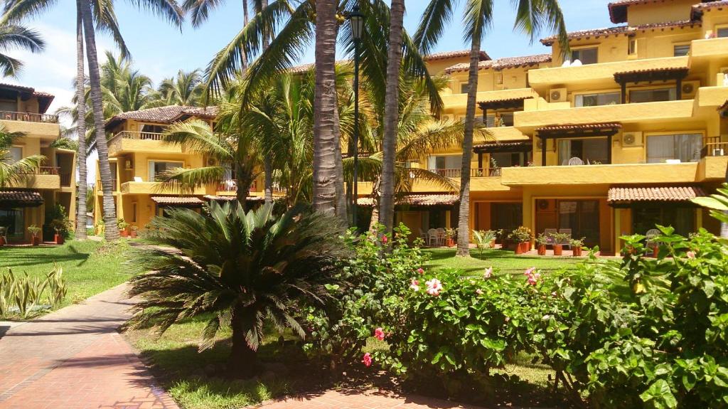 un grand bâtiment jaune avec des palmiers et un trottoir dans l'établissement Villas del Sol en Los Tules, à Puerto Vallarta