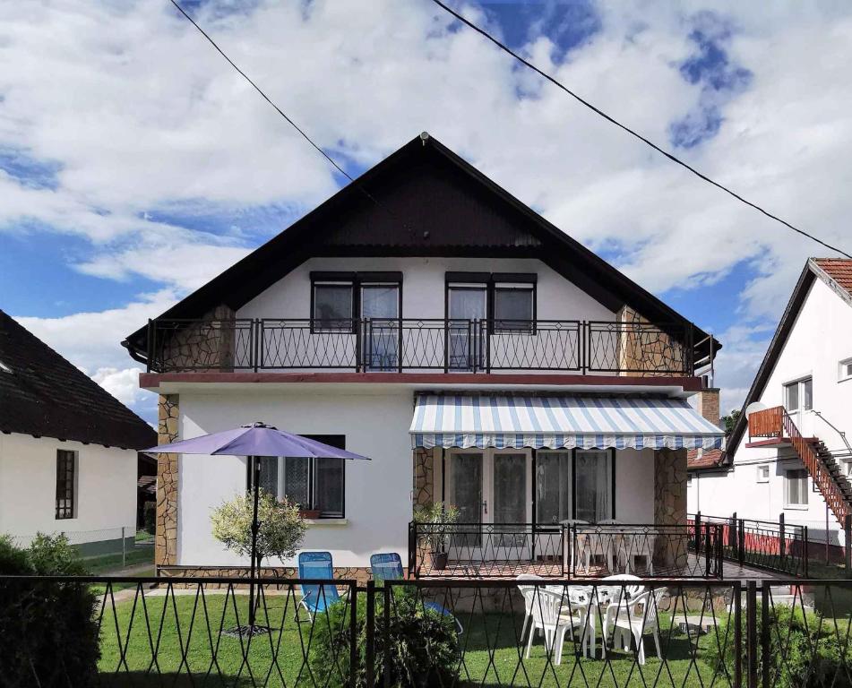 a white house with a balcony with tables and an umbrella at Holiday home in Balatonkeresztur 19387 in Hegy