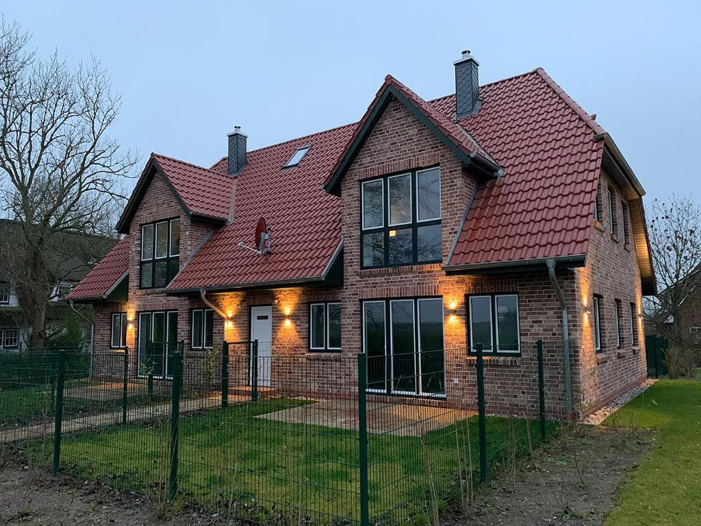 a brick house with a red roof and a fence at Dünentraum, Ferienwohnung für 4 Personen - Erwachsene oder Kinder - in DE FEERJENHUSEN am Haubarg von Vollerwiek, Fertigstellung April 2020 in Vollerwiek