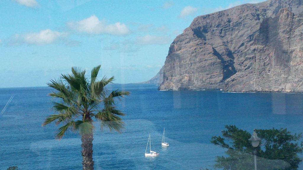 a painting of a palm tree and boats in the water at Enjoy Holiday-Wonderful Views in Acantilado de los Gigantes