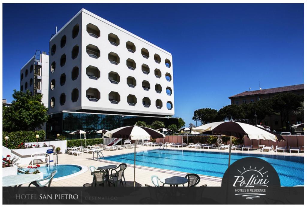 a hotel swimming pool with tables and umbrellas and a building at Hotel San Pietro in Cesenatico