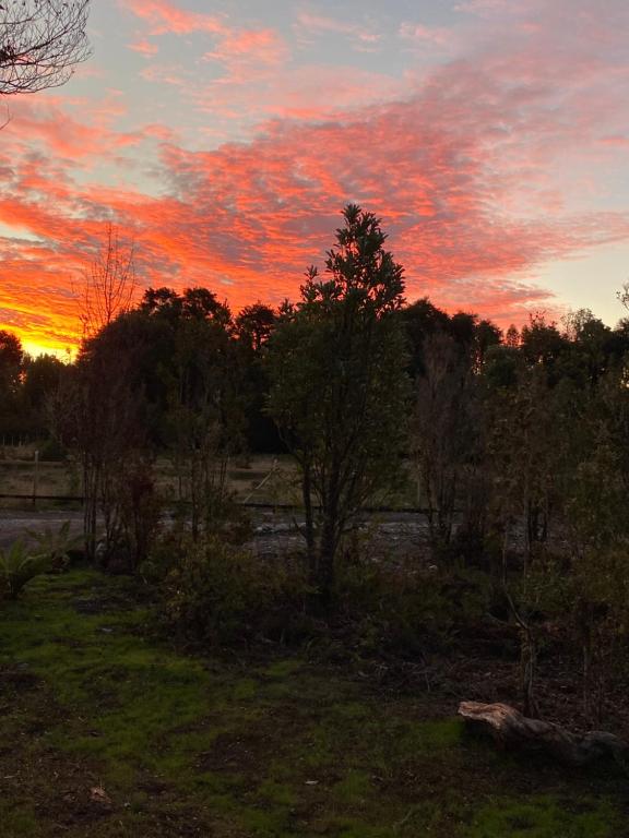 una puesta de sol sobre un campo con árboles y un río en Cabañas Mi Refugio Puerto Varas, en Puerto Varas