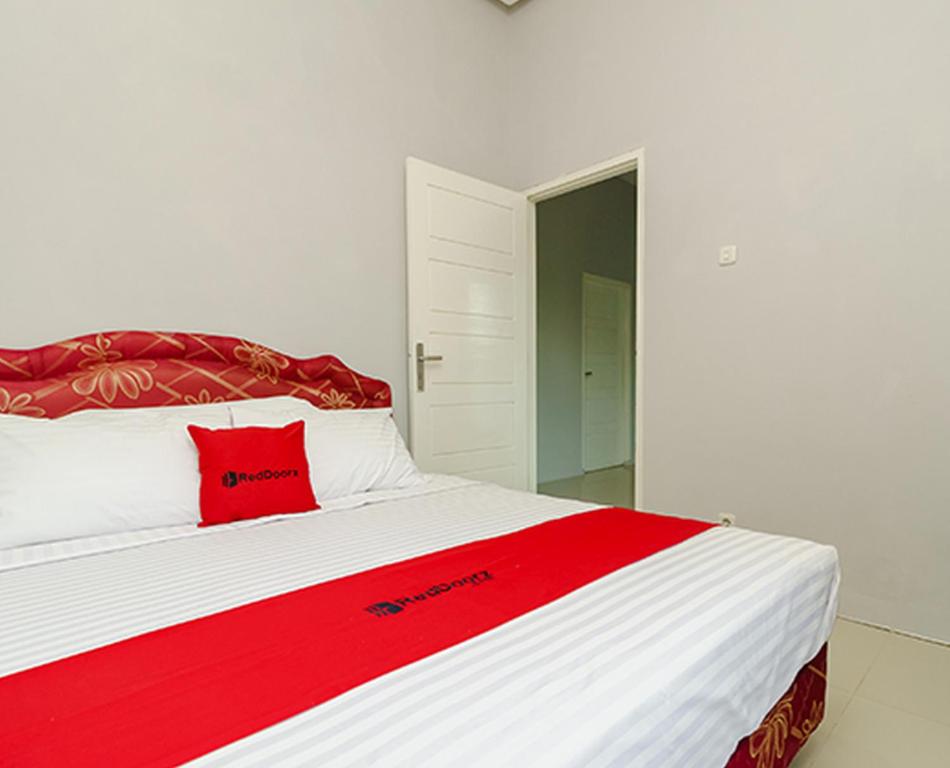 Un dormitorio con una almohada roja en una cama blanca en RedDoorz @ Jalan Demang Lebar Raya Palembang en Palembang