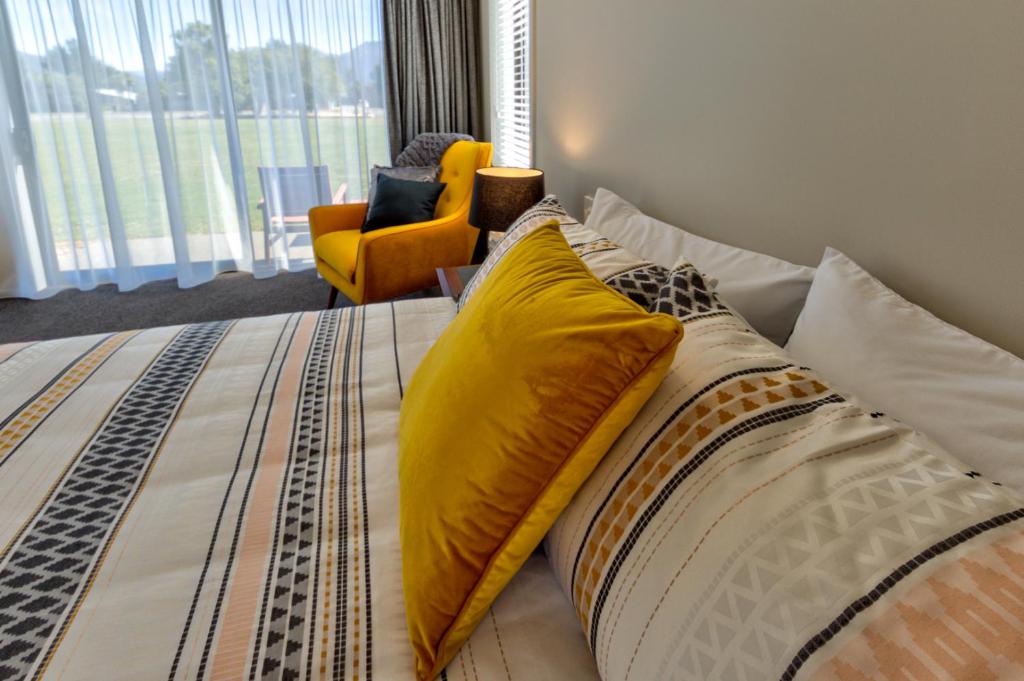 een slaapkamer met een bed met gele kussens en een stoel bij Annies on Milford in Te Anau