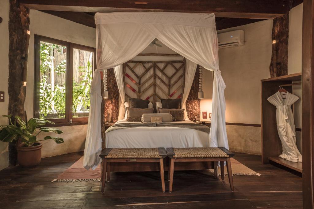 a bedroom with a canopy bed with a bench and a table at Delek Tulum in Tulum