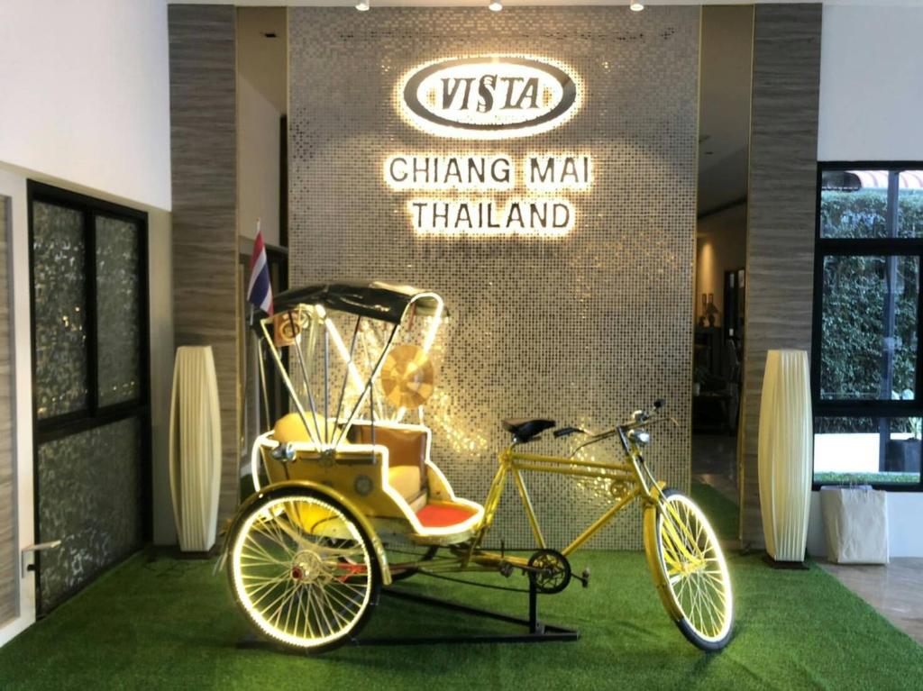 A gold bicycle rickshaw displayed beneath the illuminated Vista Chiang Mai sign.