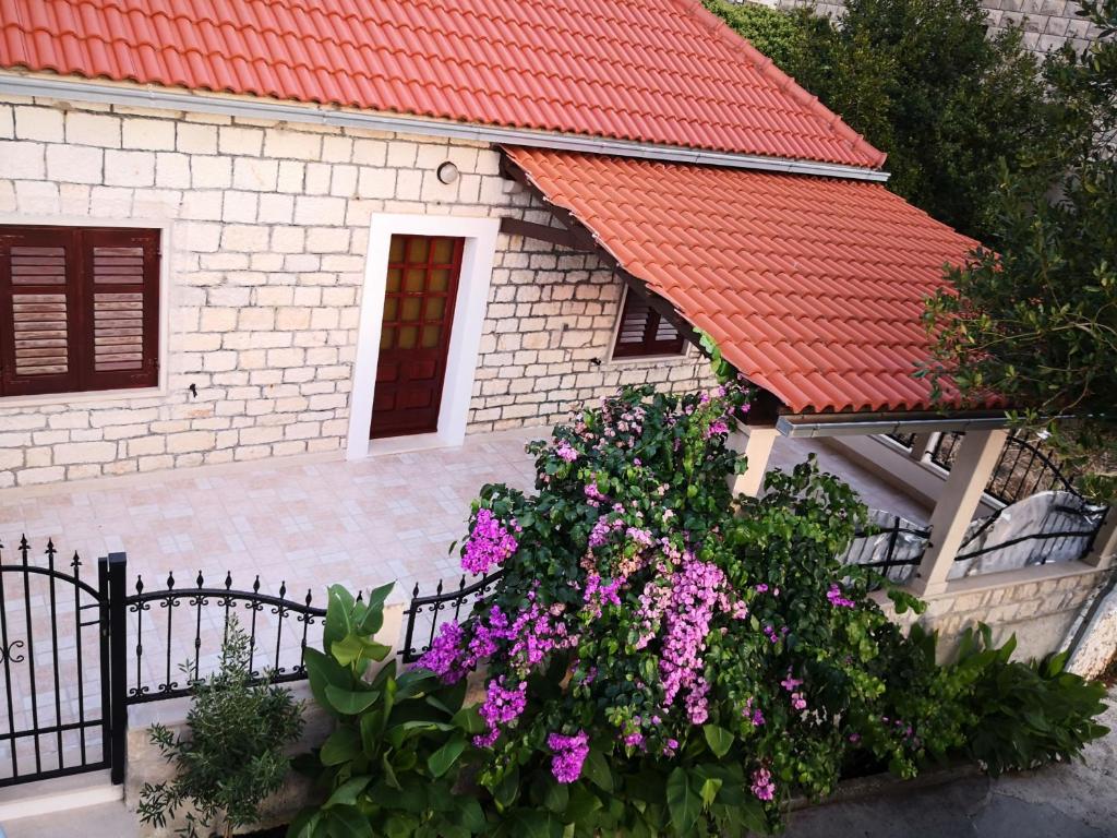 una casa con techo rojo y flores moradas en apartman house Bjedov, en Povlja
