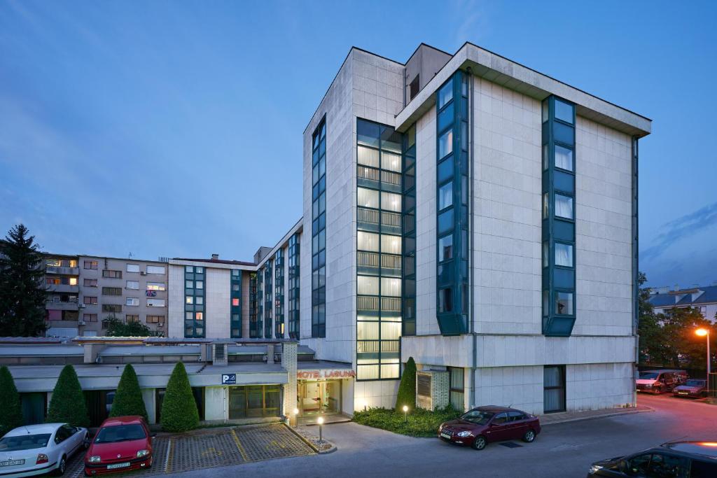 Un grand bâtiment avec des voitures garées dans un parking dans l'établissement Hotel Laguna Zagreb, à Zagreb