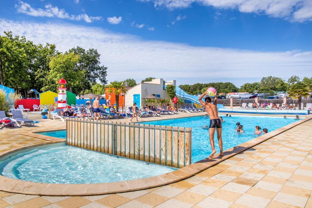 un homme debout dans une piscine dans un parc d'attractions dans l'établissement Mobil Home XXL 4 chambres - Camping Le Domaine d'Oléron, à Foulerot