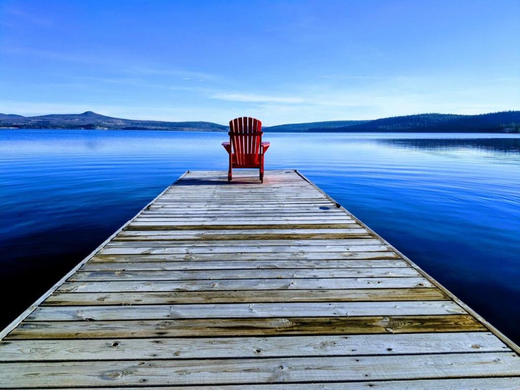 a red chair sitting on a dock on a lake at Barney’s Lakeside Resort in Puntzi Lake