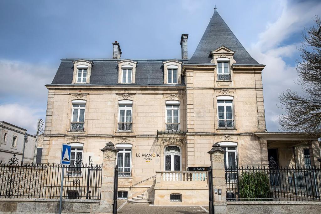 un grand bâtiment en pierre avec une clôture noire dans l'établissement Le Manoir Hôtel, à La Rochelle