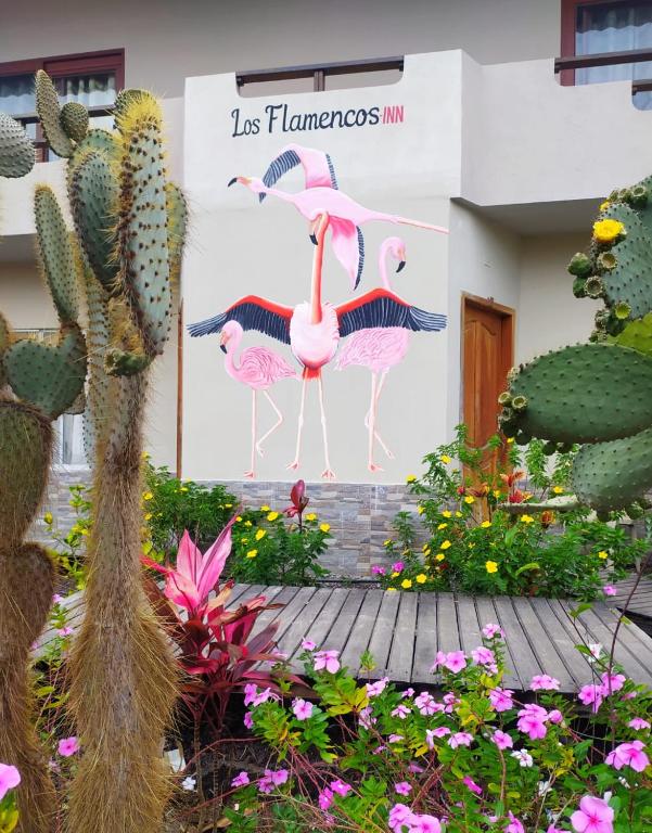 a sign with three flamingos in a garden with flowers at Hostal Los Flamencos in Puerto Villamil