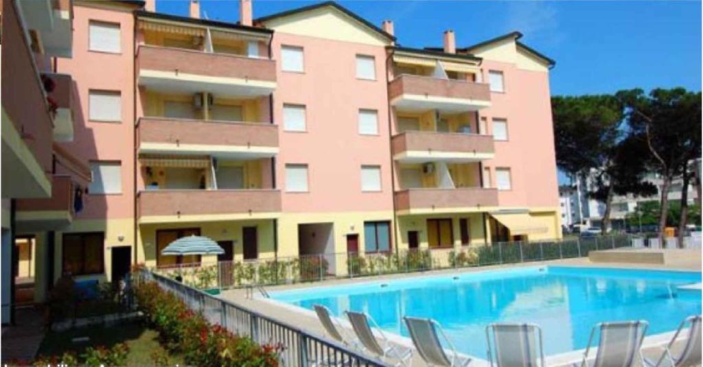 ein großes rosafarbenes Gebäude mit Pool und Stühlen in der Unterkunft Apartment in Rosolina Mare 25066 in Rosolina Mare