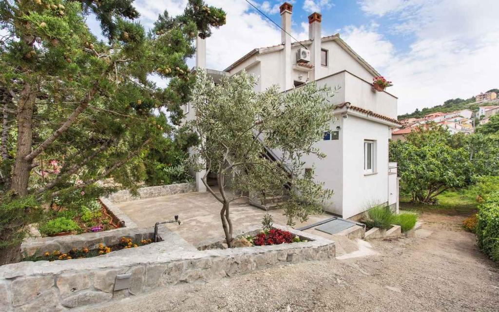 a white house with trees and flowers in front of it at Apartments in Vrbnik/Insel Krk 36005 in Vrbnik