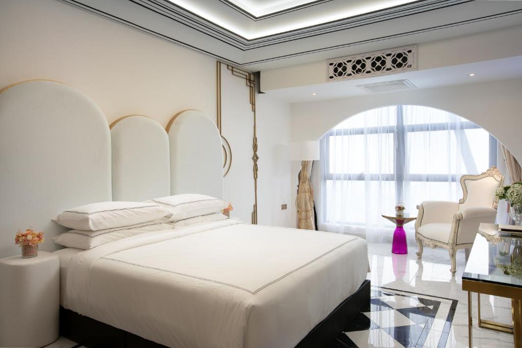 A white bedroom with an arched window, large bed, armchair and small table.
