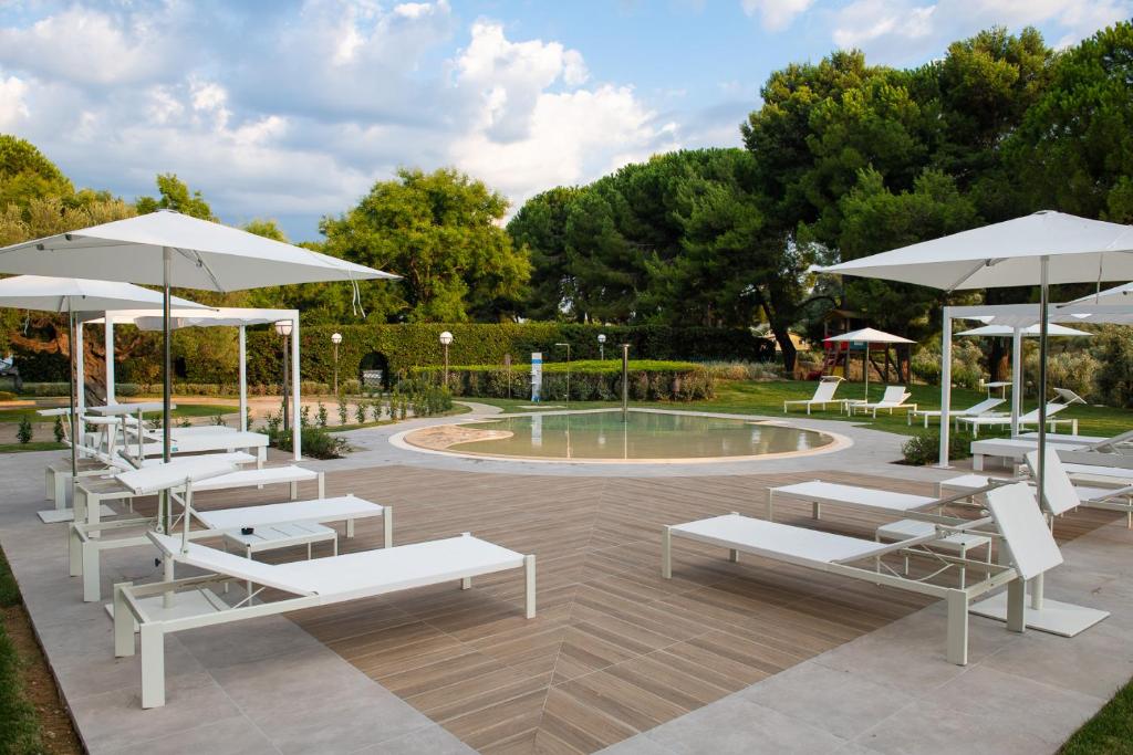 a patio with white benches and umbrellas next to a pool at Villa Maria Hotel & SPA in Francavilla al Mare