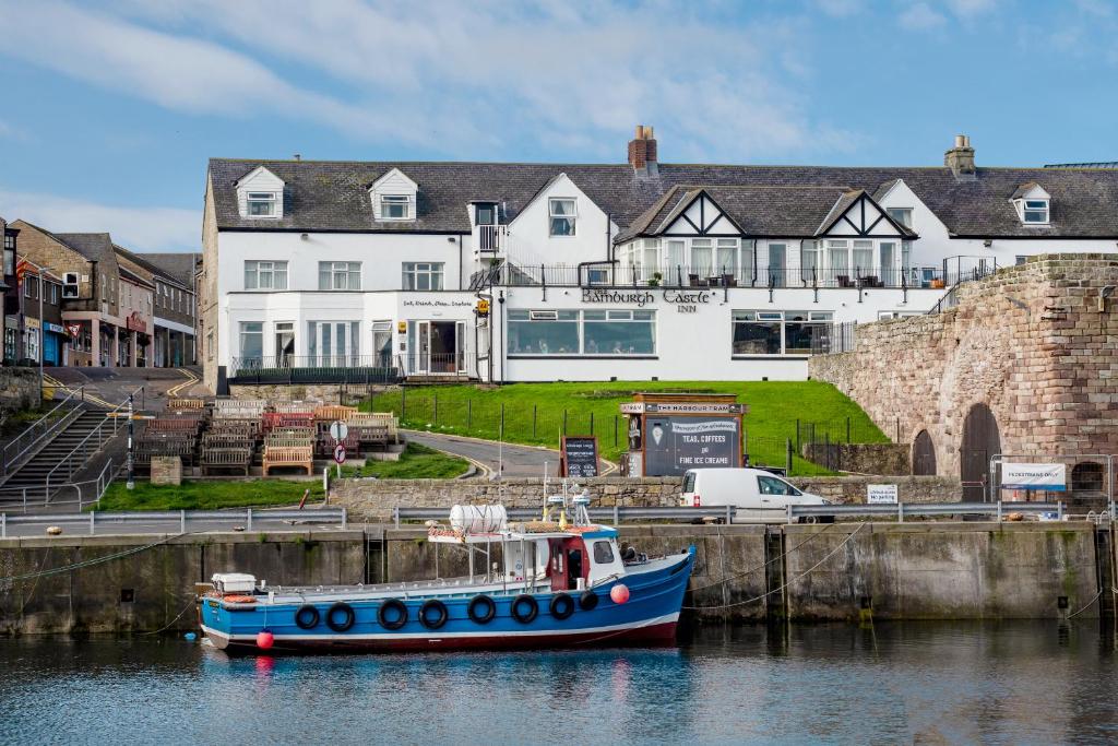 um barco azul ancorado na água em frente a uma casa em The Bamburgh Castle Inn - The Inn Collection Group em Seahouses