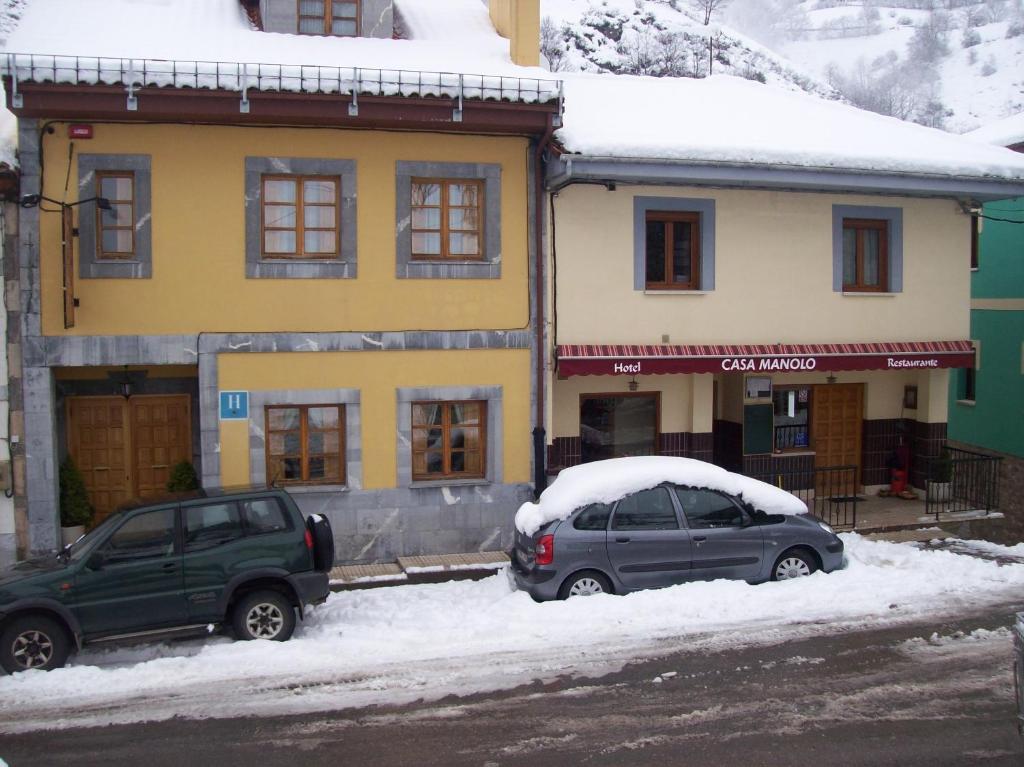 dos autos estacionados frente a una casa con nieve en Hotel Restaurante Casa Manolo en Páramo