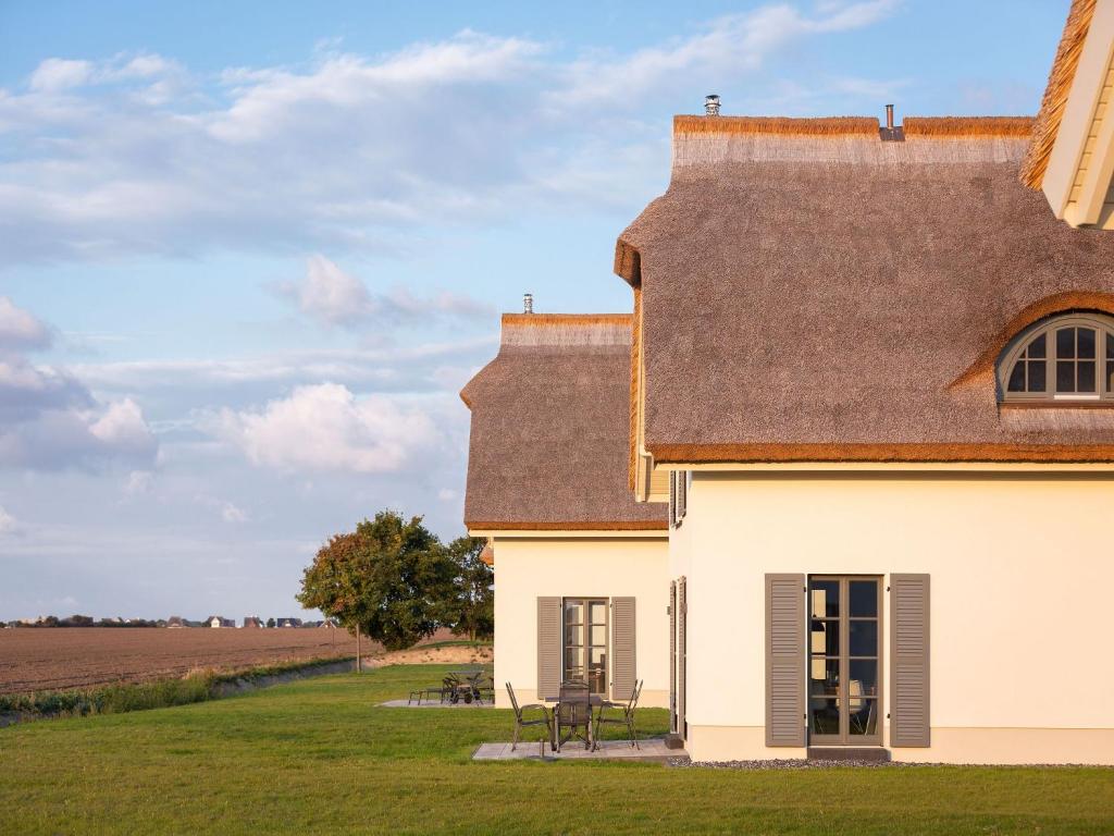 a white house with a brown roof and a field at Reetland am Meer - Premium Reetdachvilla mit 2 Schlafzimmern, Sauna und Kamin E04 in Dranske