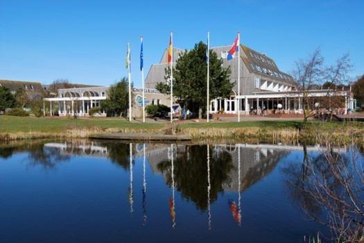 a large building with a reflection in a body of water at Heerlijk App APHRODITE - beg grond met TERRAS, eigen KEUKEN, Incl Verwarmd Hotel-ZWEMBAD, nabij Strand en Vuurtoren in Hollum