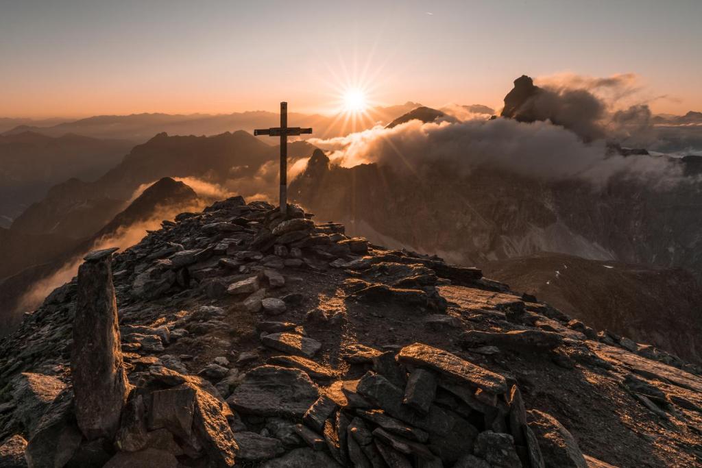 a cross on the top of a mountain at sunset at Apartments Ban Guggugg in Colle Isarco