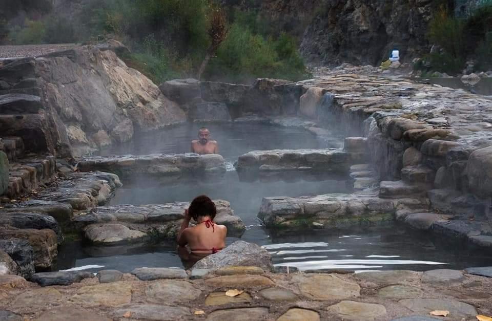 a woman sitting in a hot spring with two men in the water at Casa Flor de lis in Herce