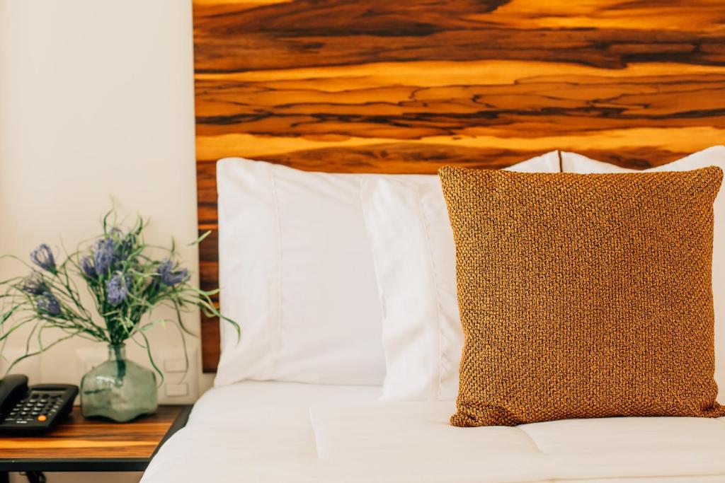 Una cama con almohadas blancas y una mesa con teléfono. en Hotel Tabáa Oaxaca en Oaxaca de Juárez