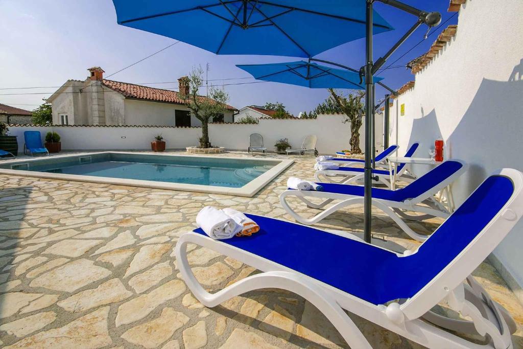 para krzeseł i parasol obok basenu w obiekcie Holiday home in Porec 35381 w mieście Dračevac
