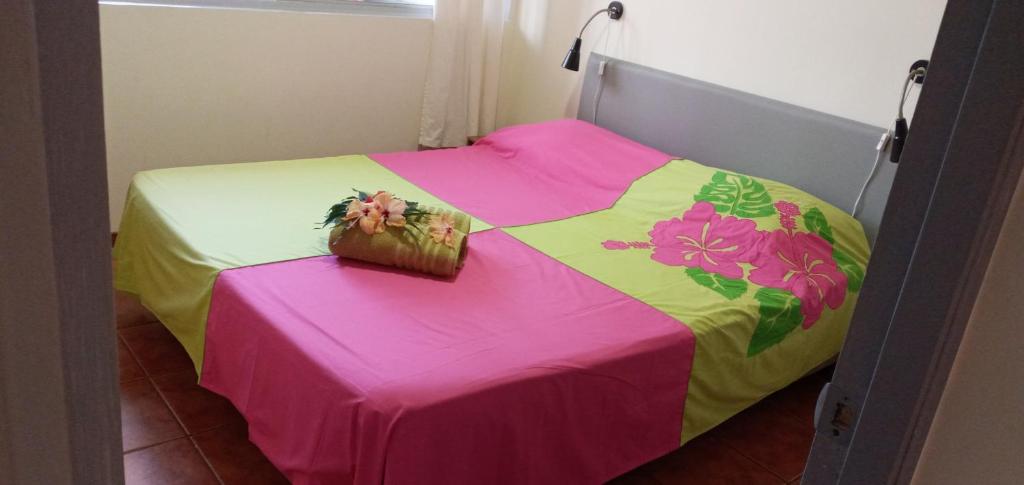 a bed with a pink and yellow blanket on it at Manuia Reva in Papeete