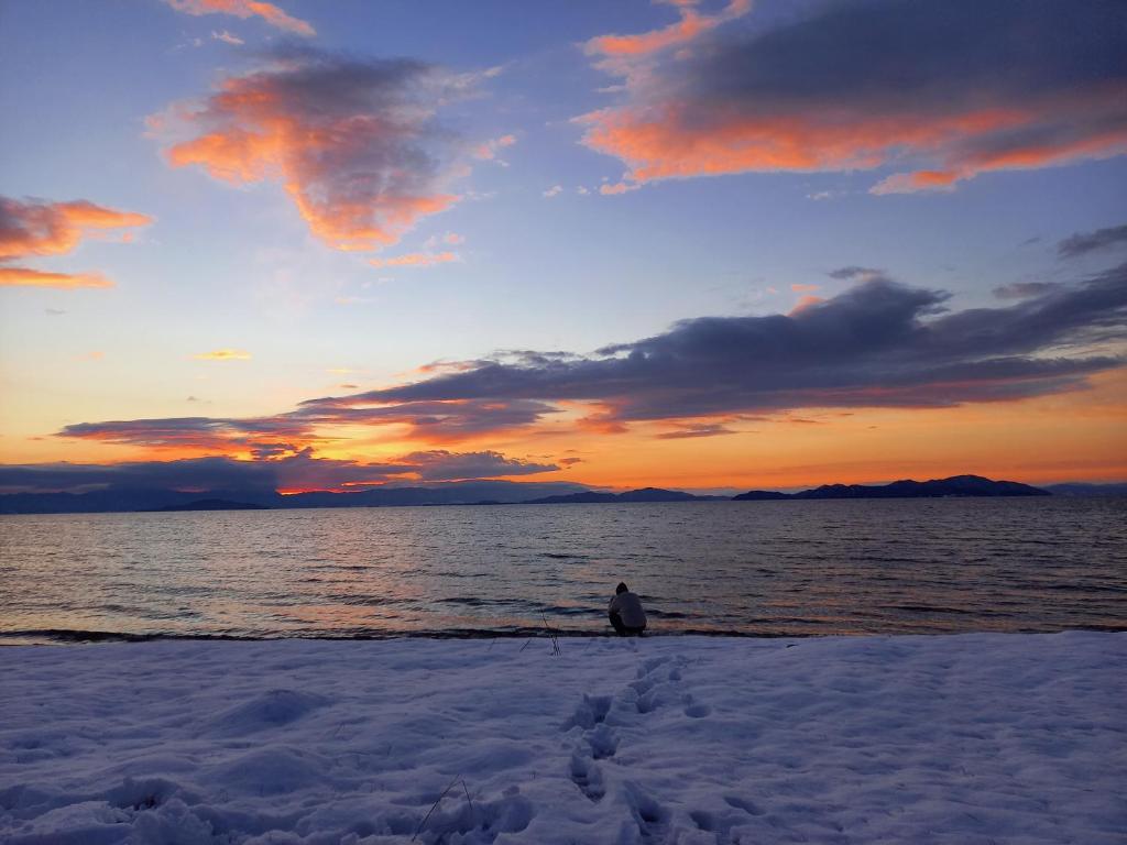 高島市にある臨湖荘の夕日を眺めながら海辺に座る者