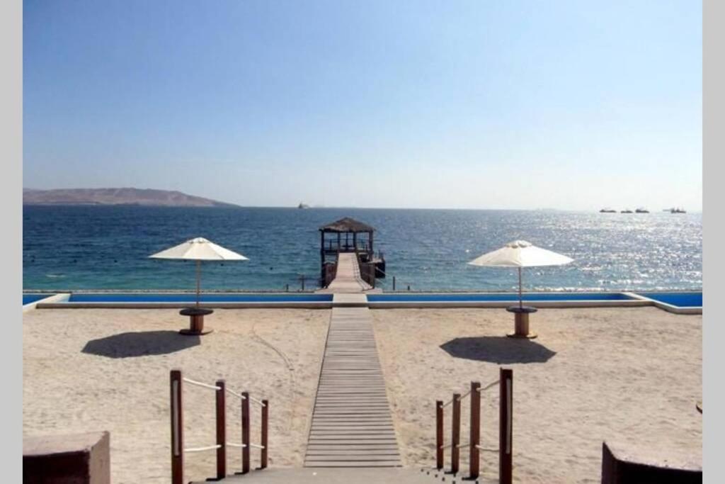a pier on the beach with umbrellas on the sand at PARACAS megaview bayfront flat in Paracas