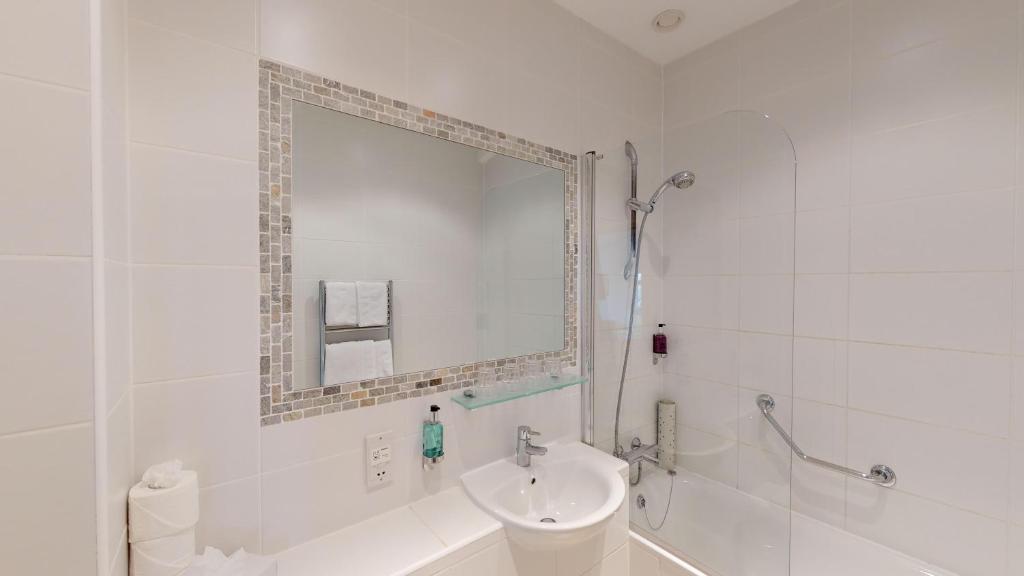 a white bathroom with a sink and a mirror at Ommaroo Hotel in Saint Helier Jersey