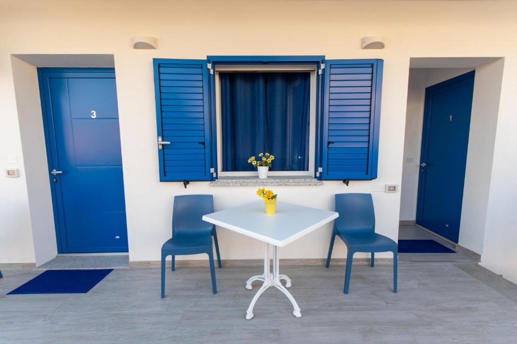 une table et des chaises blanches avec des fenêtres à volets bleus dans l'établissement Bed & Blu, à La Caletta