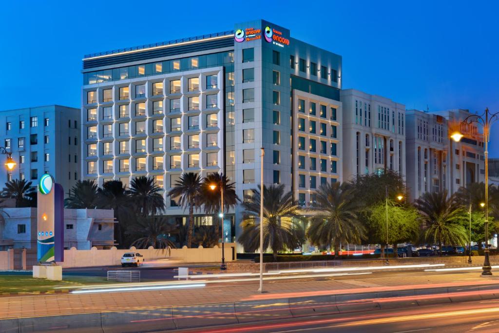 a large building with palm trees in front of a street at Ramada Encore by Wyndham Muscat Al-Ghubra in Muscat