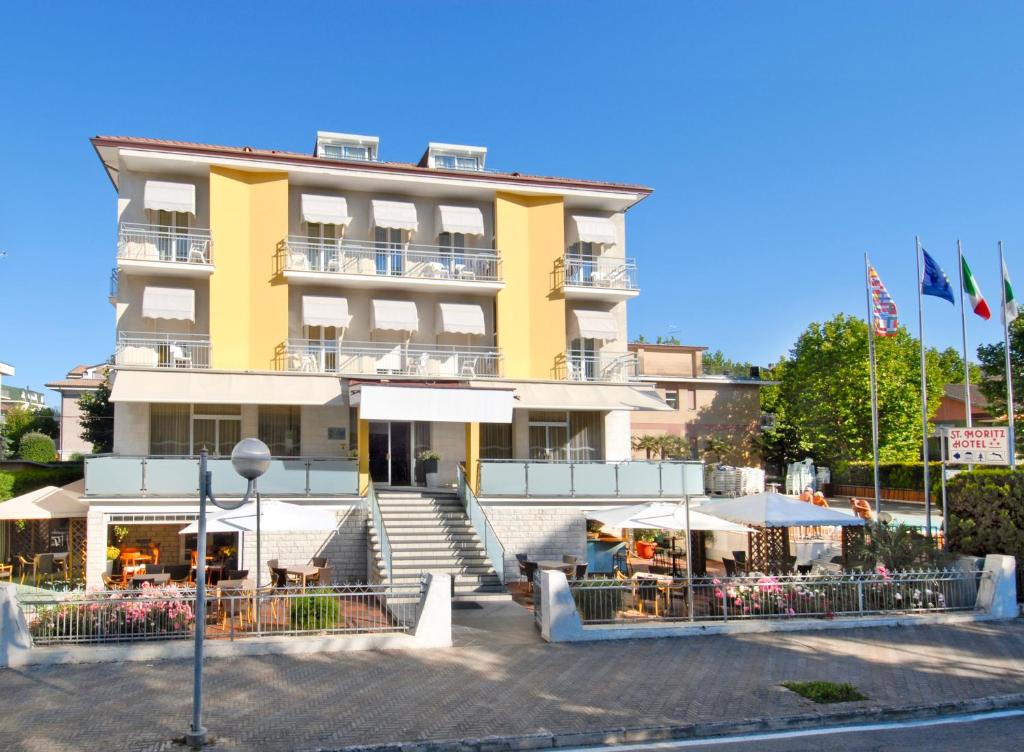 a yellow building with tables and umbrellas in front of it at Hotel St. Moritz in Bellaria-Igea Marina