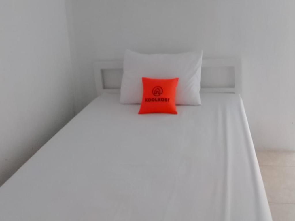 Ein rotes Kissen liegt auf einem weißen Bett. in der Unterkunft Koolkost near DPRD Kabupaten Subang in Subang