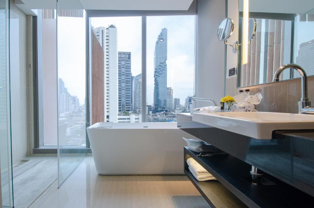 a bathroom with a tub and a sink and a large window at Amara Bangkok Hotel in Bangkok