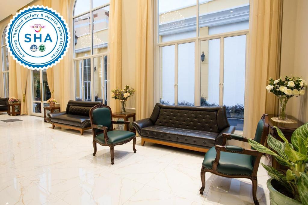 A window-lined lounge with leather sofas, green armchairs and decorative plants.