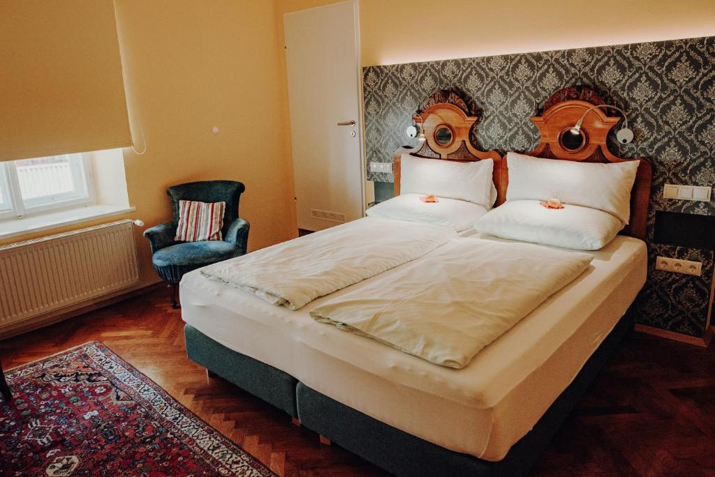 ein Schlafzimmer mit einem großen Bett und einem Stuhl in der Unterkunft Gasthof Eberhard - Hof, Wirtshaus & Herberge in Sankt Michael in Obersteiermark