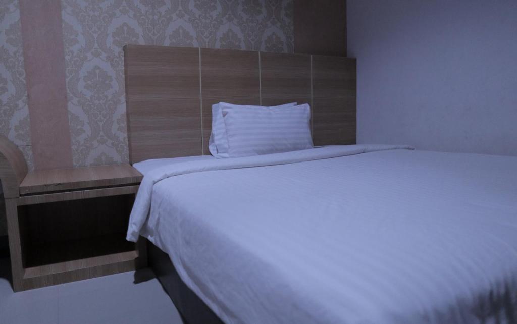 a bedroom with a white bed with a wooden headboard at RedDoorz @ Pasangkayu Mamuju Utara in Pasangkayu