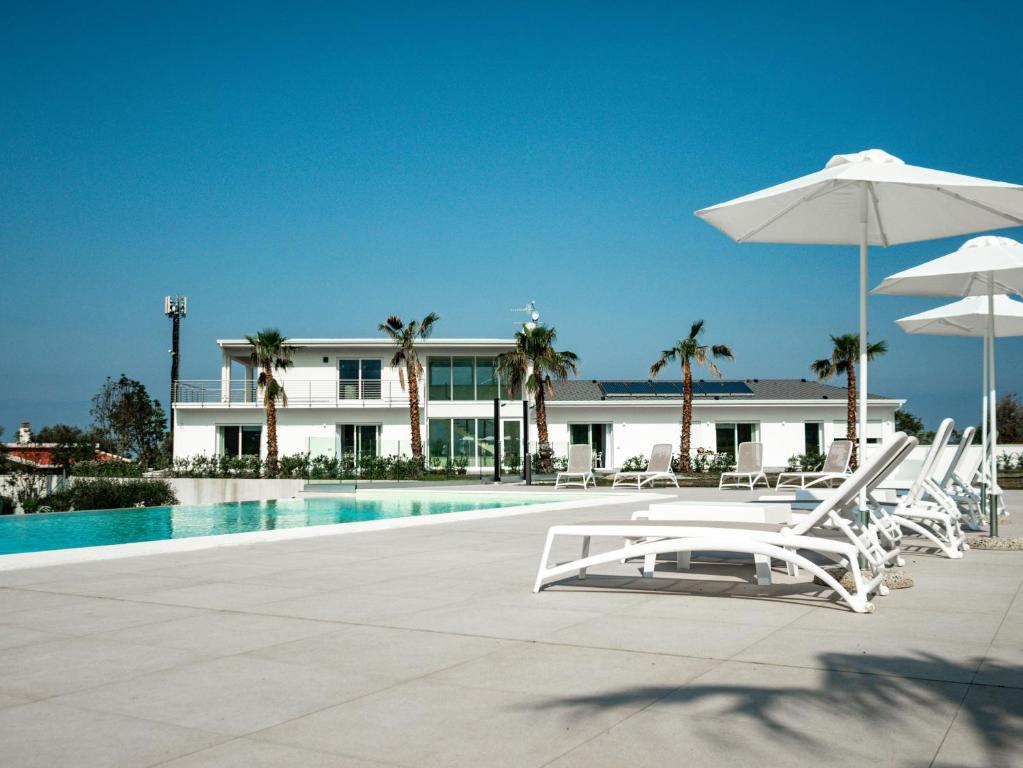 a pool with chairs and umbrellas in front of a building at Resilienza Apartment in Capo dʼOrlando
