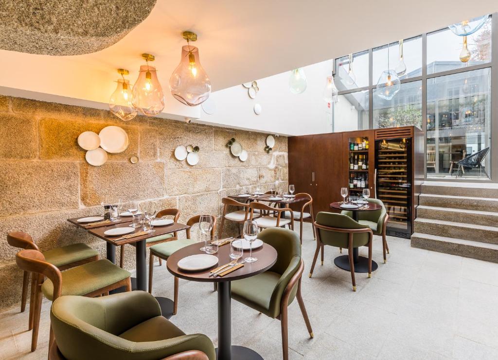 Chic boutique hotel dining area with a mix of mid-century modern and contemporary furniture, round wooden tables, olive-green velvet chairs, and natural light pouring in from a skylight and glass doors