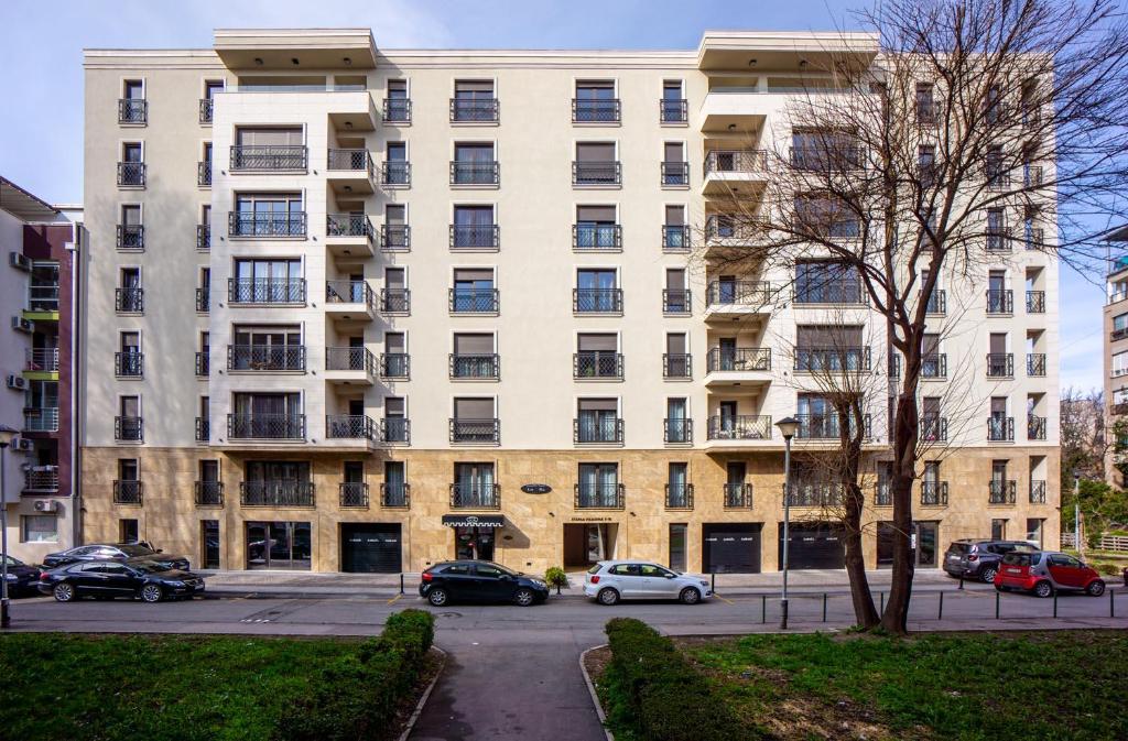 a large white building with cars parked in a parking lot at Hotel LoRa in Belgrade