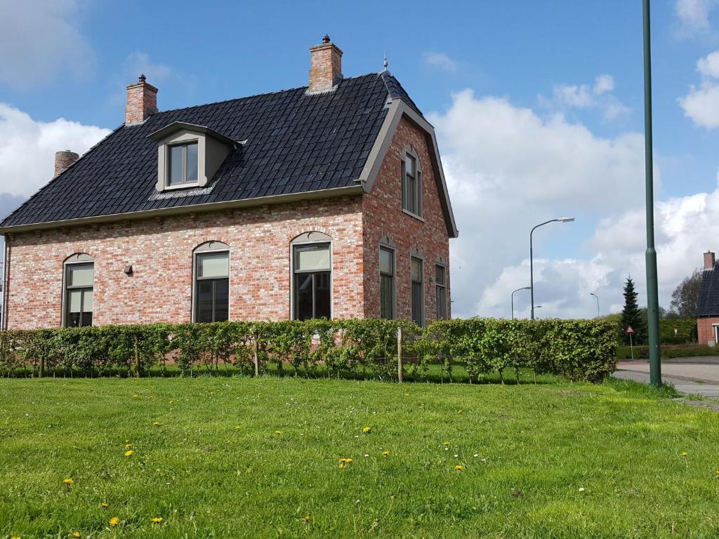 une maison en briques avec un toit noir sur une cour verdoyante dans l'établissement Fisherman s house near the Lauwersmeer, à Zoutkamp