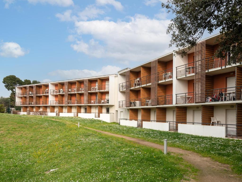 an apartment building with balconies and a grass field at Vacancéole - Le Fonserane - Béziers Sud in Béziers