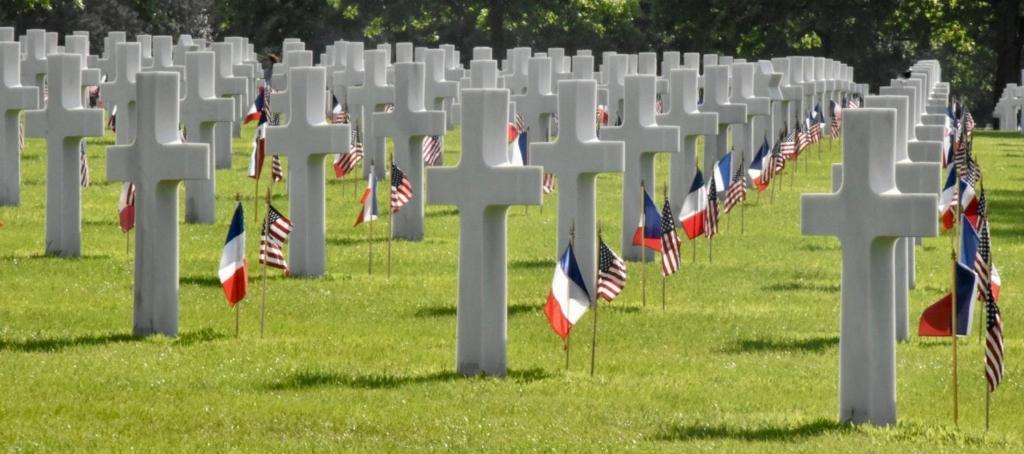 a row of graves with american flags in the grass at Villa kahlo Omaha Beach in Colleville-sur-Mer