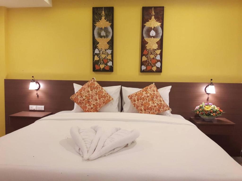 A double bed with orange patterned cushions, Thai artwork, and a folded towel decoration.