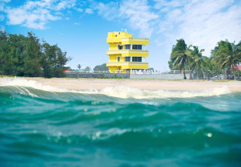 - un bâtiment jaune sur la plage à côté de l'océan dans l'établissement Pranaav Beach Resort, à Pondichéry