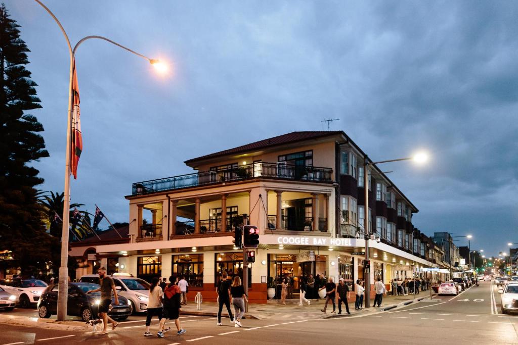 um grupo de pessoas atravessando uma rua em frente a um edifício em Coogee Bay Hotel em Sidney