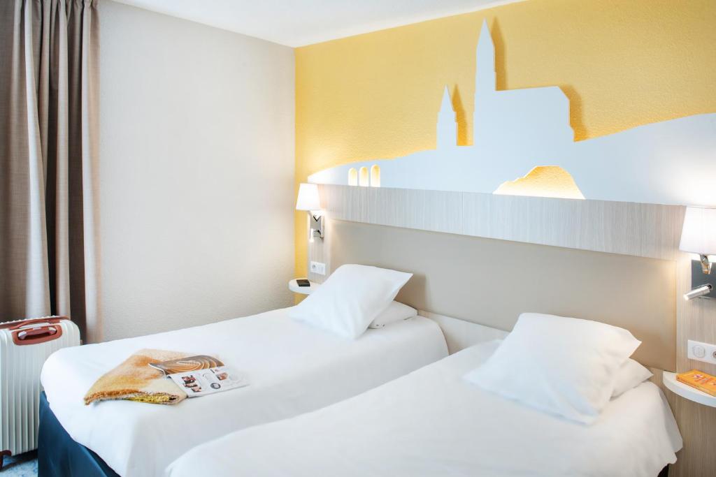 Dos camas en una habitación de hotel con un bolso en la parte superior en Hôtel Saint Sauveur, en Lourdes